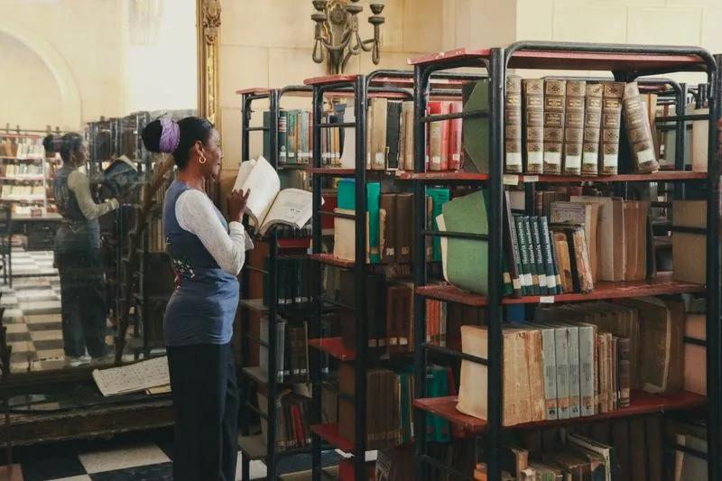 Woman leafing through an old book in front of metal shelves stacked with bound volumes in a library