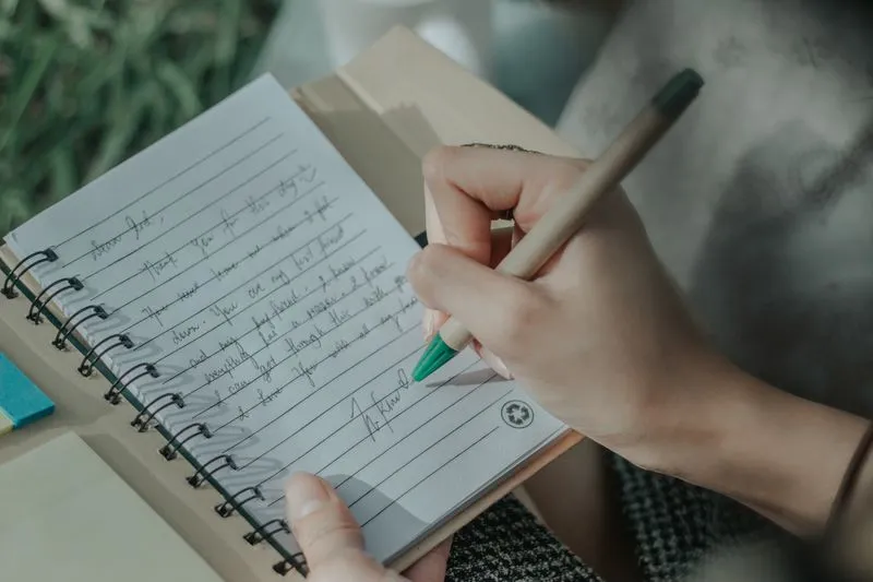 Hand writing a short thank-you note in pen in a spiral notebook