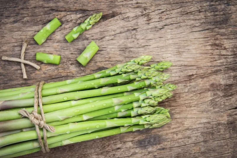 Bunch of green asparagus tied with twine, with a few cut pieces, on a wooden board