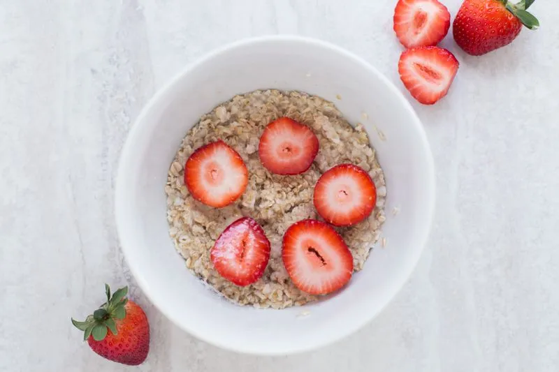 Bowl of oats topped with halved strawberries on a white worktop