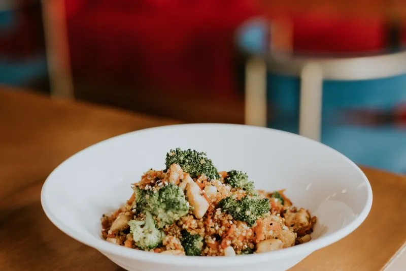 Bowl of quinoa with chicken, broccoli, shredded carrot and sesame seeds, served in a restaurant