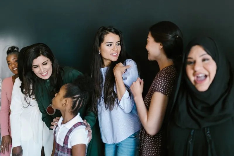 Group of women of different ages and backgrounds chatting and laughing together, a little girl among them