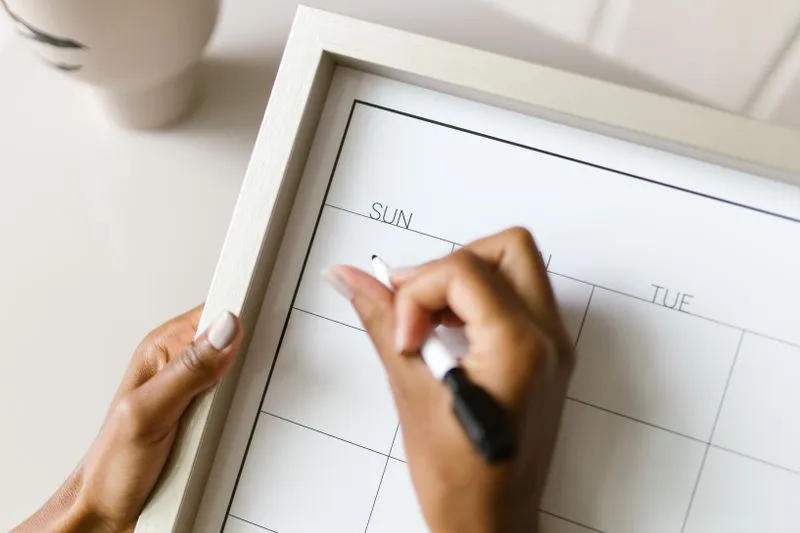 A woman's hands writing with a marker pen on a blank weekly planner board