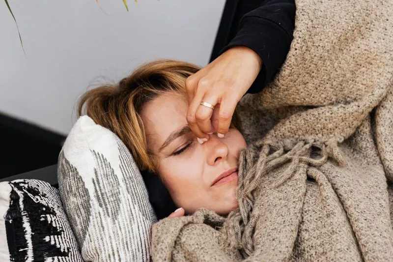 Young woman lying under a wool blanket, eyes closed, her face tight with pain