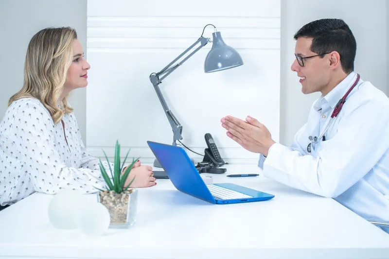 Doctor in a white coat talking with a patient seated across his desk