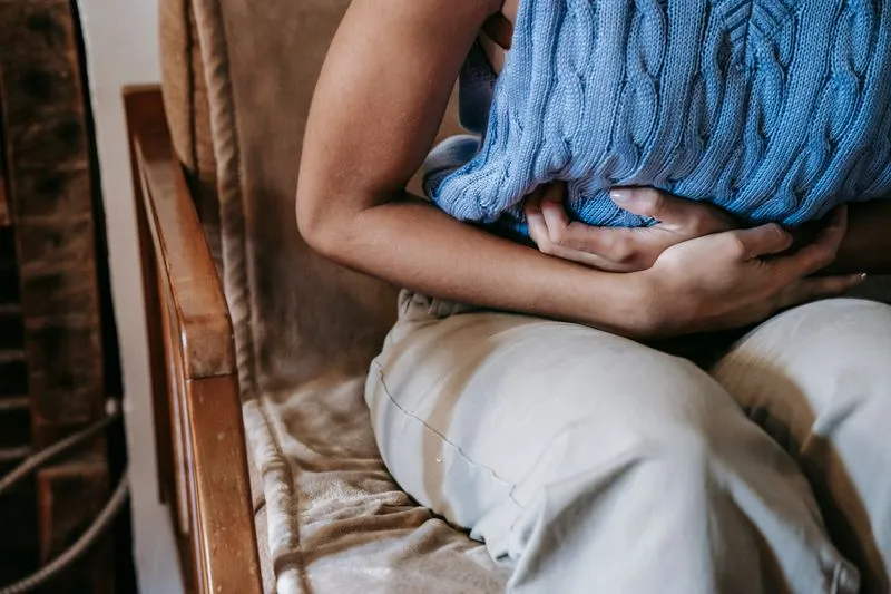 Woman seated in a wooden armchair, both hands pressing a blue cable-knit cushion against her stomach