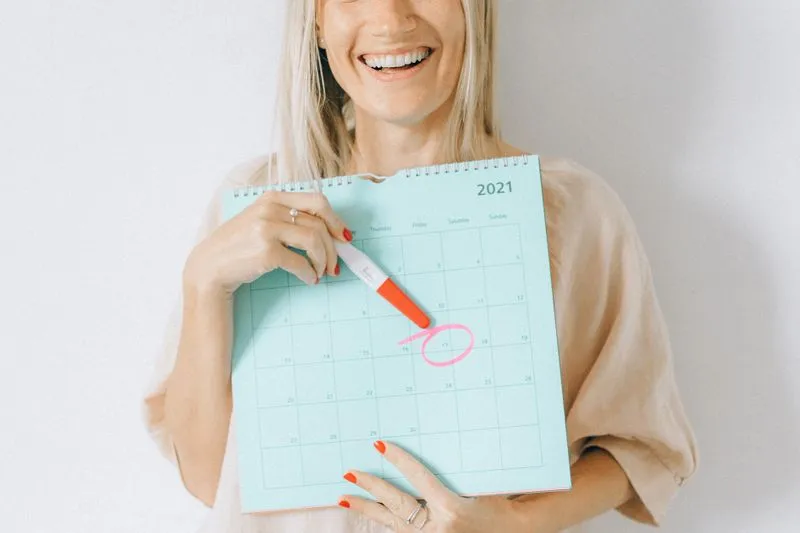 Smiling woman holding a calendar and a test, with a date circled