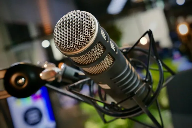 Close-up of a broadcast microphone in a shock mount, with studio lights blurred behind it