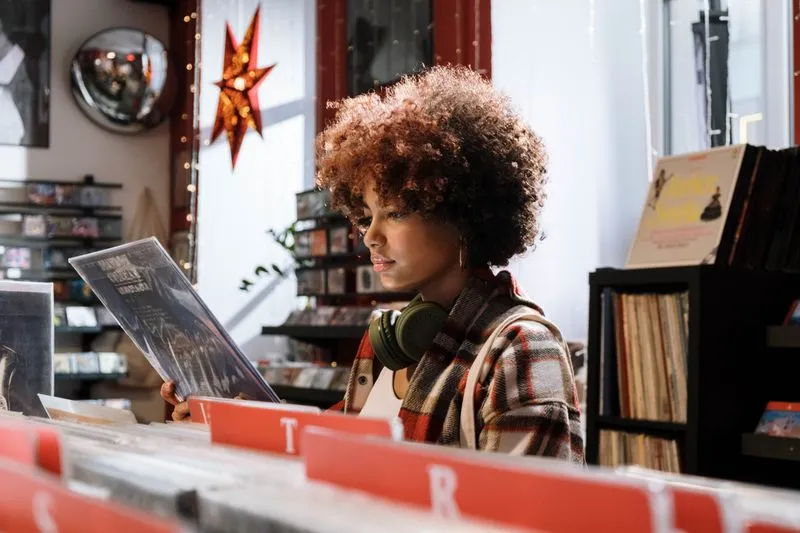 Young woman with headphones round her neck reading the back of a vinyl record in a record shop