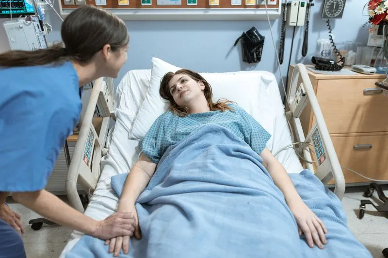 Nurse in blue scrubs reassuring a young woman lying in a hospital bed