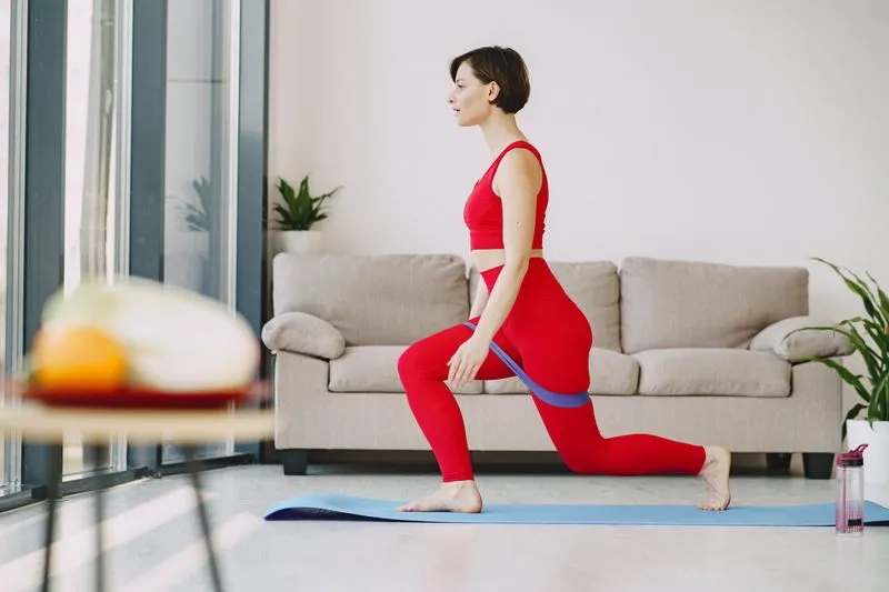 Woman in red sportswear doing a lunge with a resistance band on a mat at home