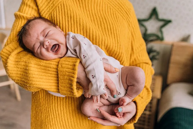 Newborn baby crying, held close in his mother's arm