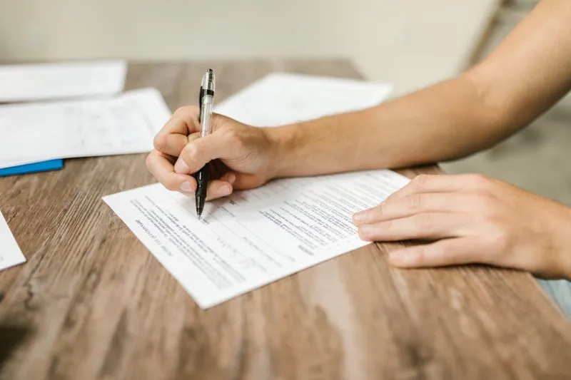 Hands filling in a printed questionnaire with a pen, on a wooden table