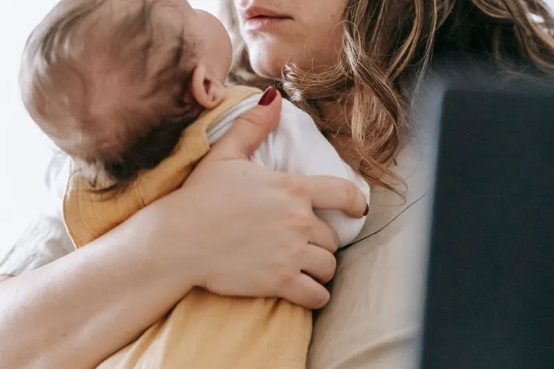 Young mother holding her newborn close, baby in a white vest and mustard romper