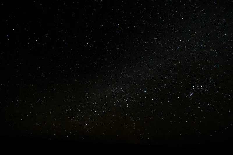 Night sky full of stars above a dark horizon, with the faint band of the Milky Way