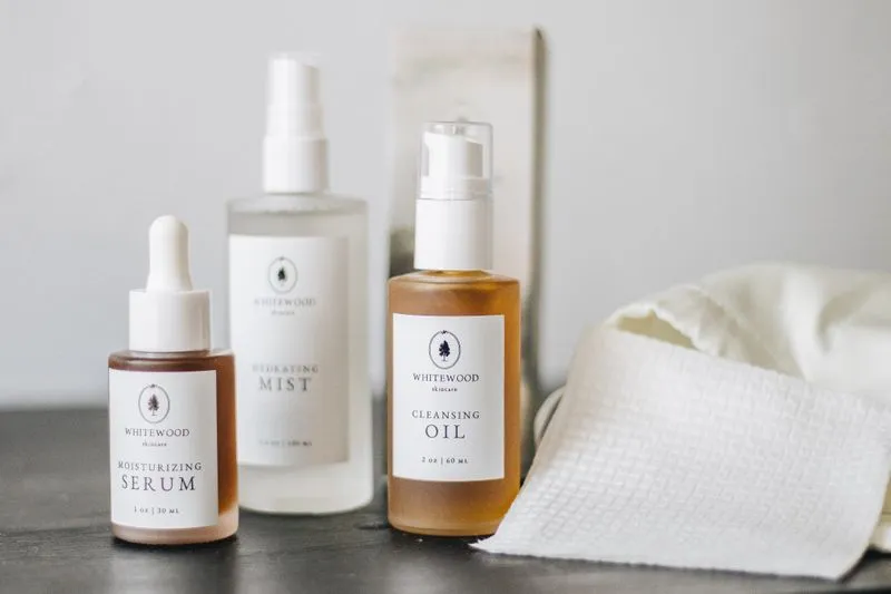 Three skincare bottles (serum, hydrating mist, cleansing oil) next to a waffle-weave cloth