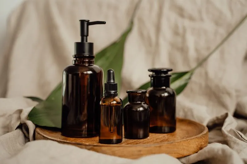 Amber glass bottles and jars of different sizes, with a green leaf, on a wooden tray
