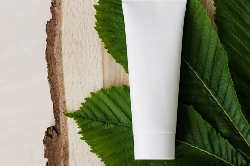 Unbranded white cream tube lying on large green leaves and a slice of wood