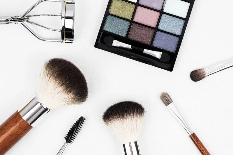 Make-up brushes, an eyeshadow palette and professional tools laid flat on white