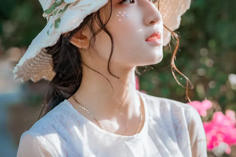 Young woman in profile under a straw hat, glowing skin in bright sunshine