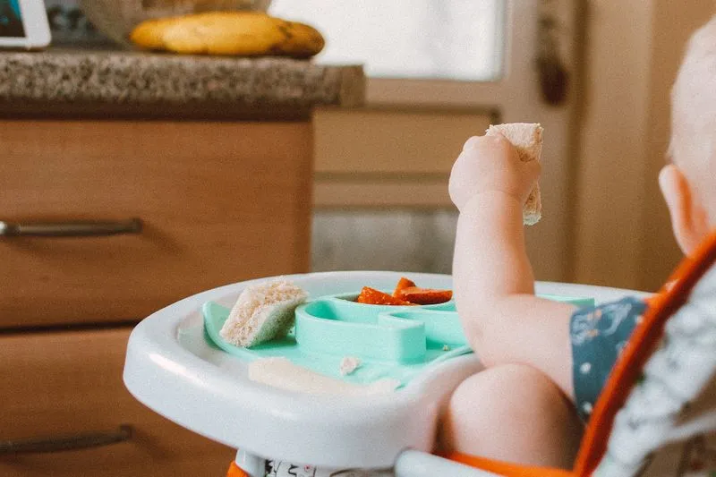 Baby doing baby-led weaning, picking up bread, with sliced strawberries on the tray