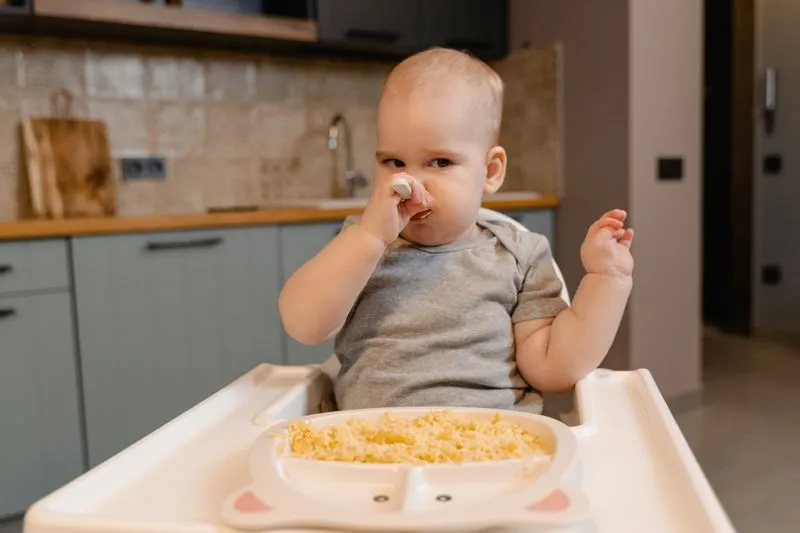 Baby sitting in a high chair tasting first foods from a spoon
