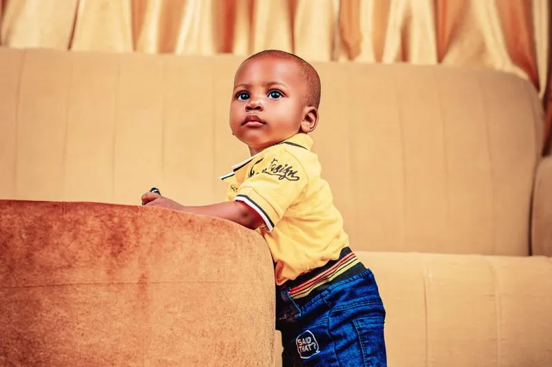 Young child standing and holding on to the arm of a sofa, looking up