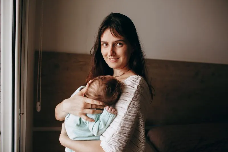 Mother holding her newborn nestled against her chest by a window