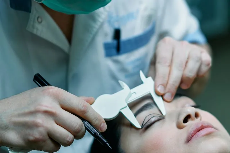Surgeon measuring a patient's eyelid with a caliper, marker pen in hand