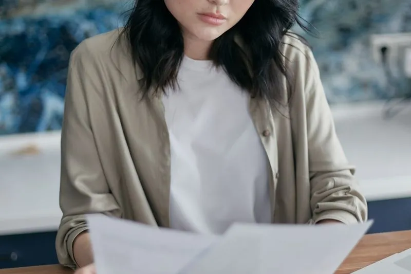 Young woman at a table reading printed pages closely