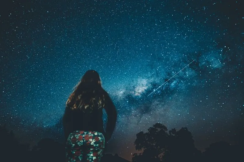 A woman seen from behind gazing at the Milky Way in a star-filled night sky