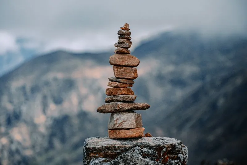 A cairn of stacked stones balanced on a rock, with misty mountains behind