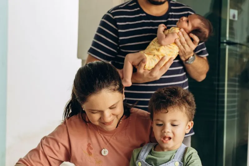 Father holding his newborn while the mother smiles with their older son