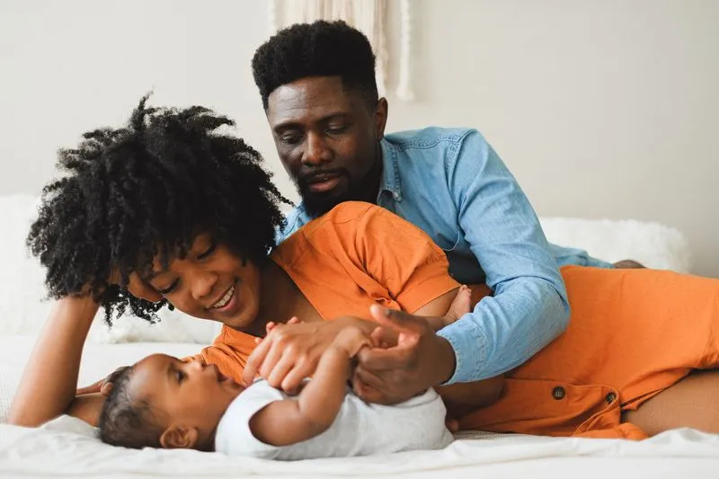 A mother and father lying on a bed, playing with their baby together