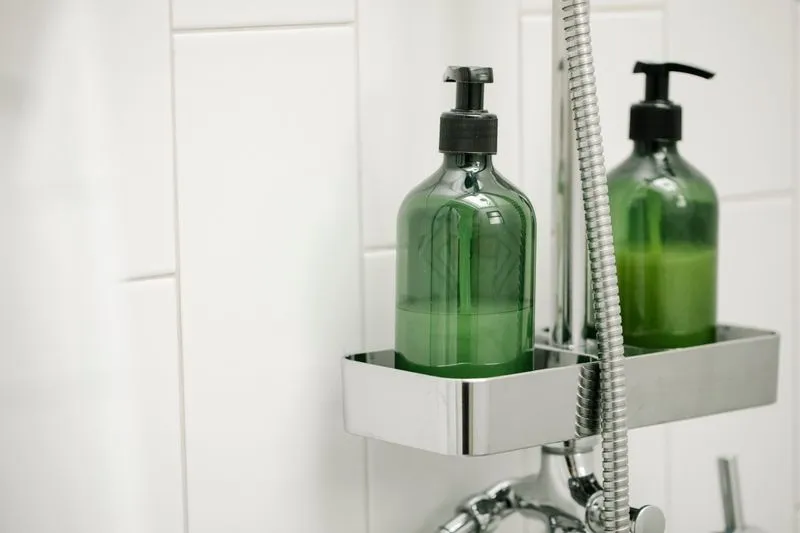Two green pump bottles on a chrome shower caddy beside the shower hose