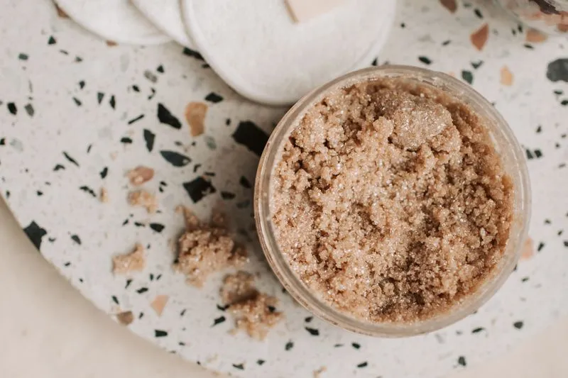 Jar of brown sugar scrub on a terrazzo tray next to reusable cotton pads