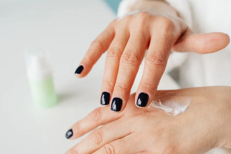 Hands with navy nail polish rubbing cream into the back of the hand