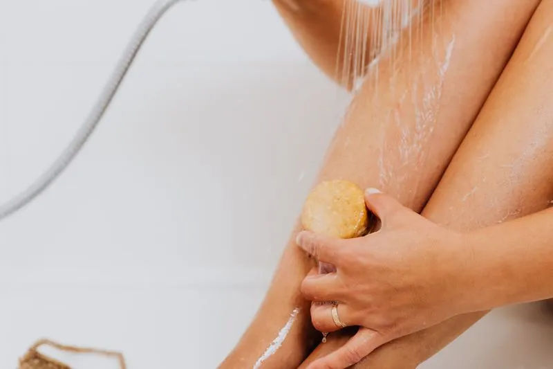 A woman rubbing a scrub bar over her leg under the shower spray