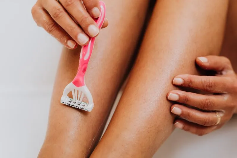 A woman running a pink razor over her wet leg