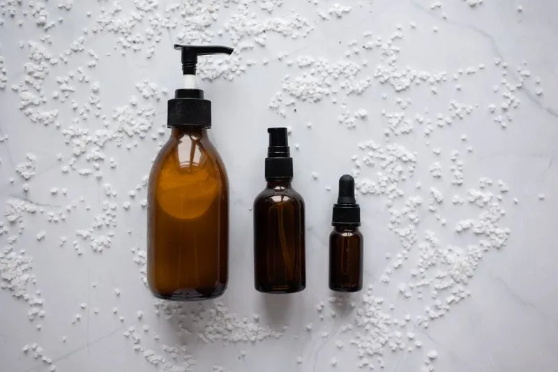 Three unlabelled amber bottles, with a pump, a spray and a dropper, on marble scattered with white crystals