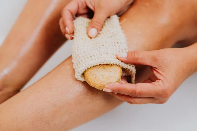 Hands scrubbing a wet leg with a sisal mitt and a bar of soap
