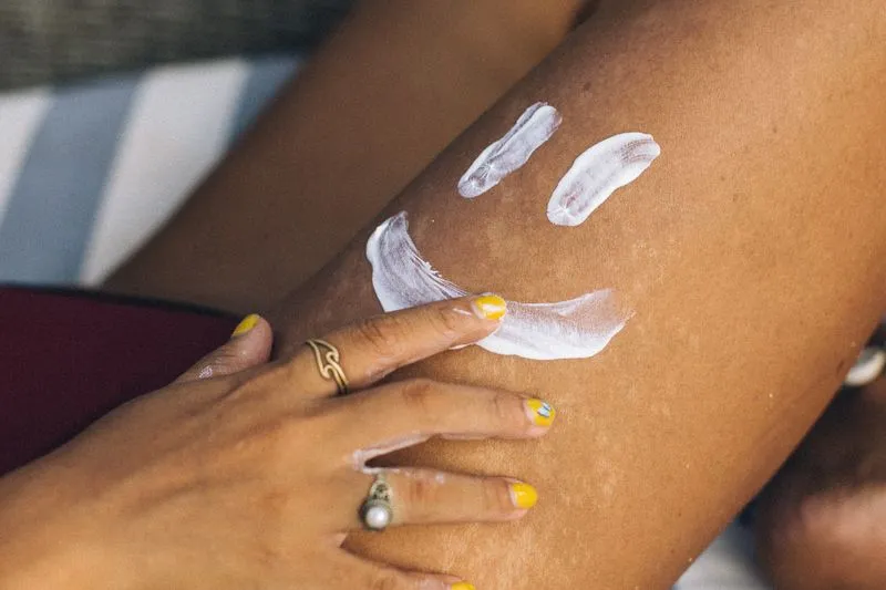 Hand with yellow-painted nails spreading white cream on a leg