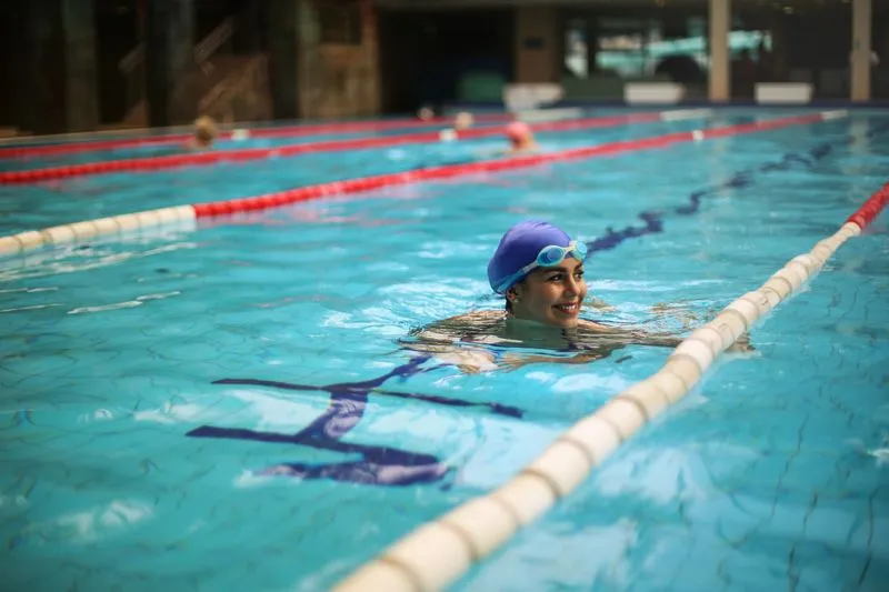 Smiling swimmer in a blue cap and goggles in the lane of an indoor pool