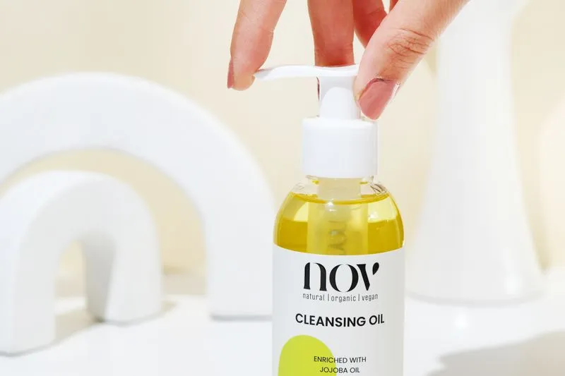 A finger pressing the pump of a bottle of cleansing oil