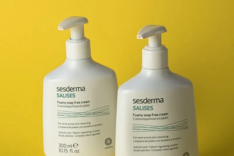 Two pump bottles of soap-free foaming cream cleanser for acne-prone skin, against a yellow background