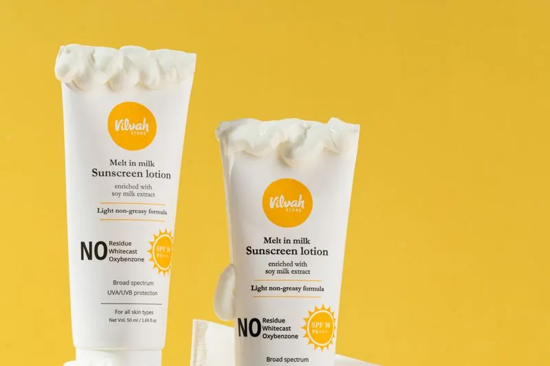 Two sunscreen tubes with their creamy texture spilling from the open cap, against a yellow background