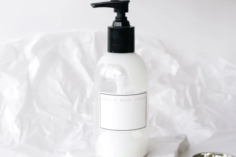 Unbranded white pump bottle labelled 'Hand & Body Cream', against crumpled tissue paper