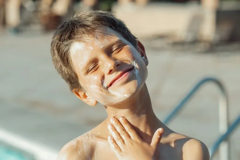 Smiling boy with a thick layer of sun cream on his face and neck by a pool