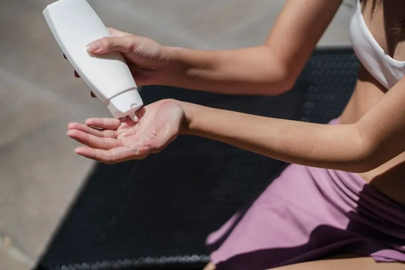 Woman in a swimsuit squeezing white lotion into her palm, sitting in the sun