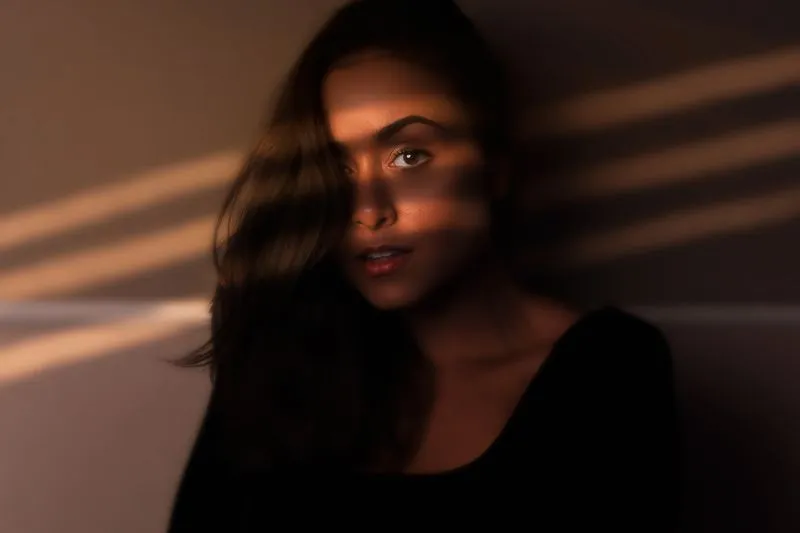 Light and shadow stripes crossing a woman's face in dim light